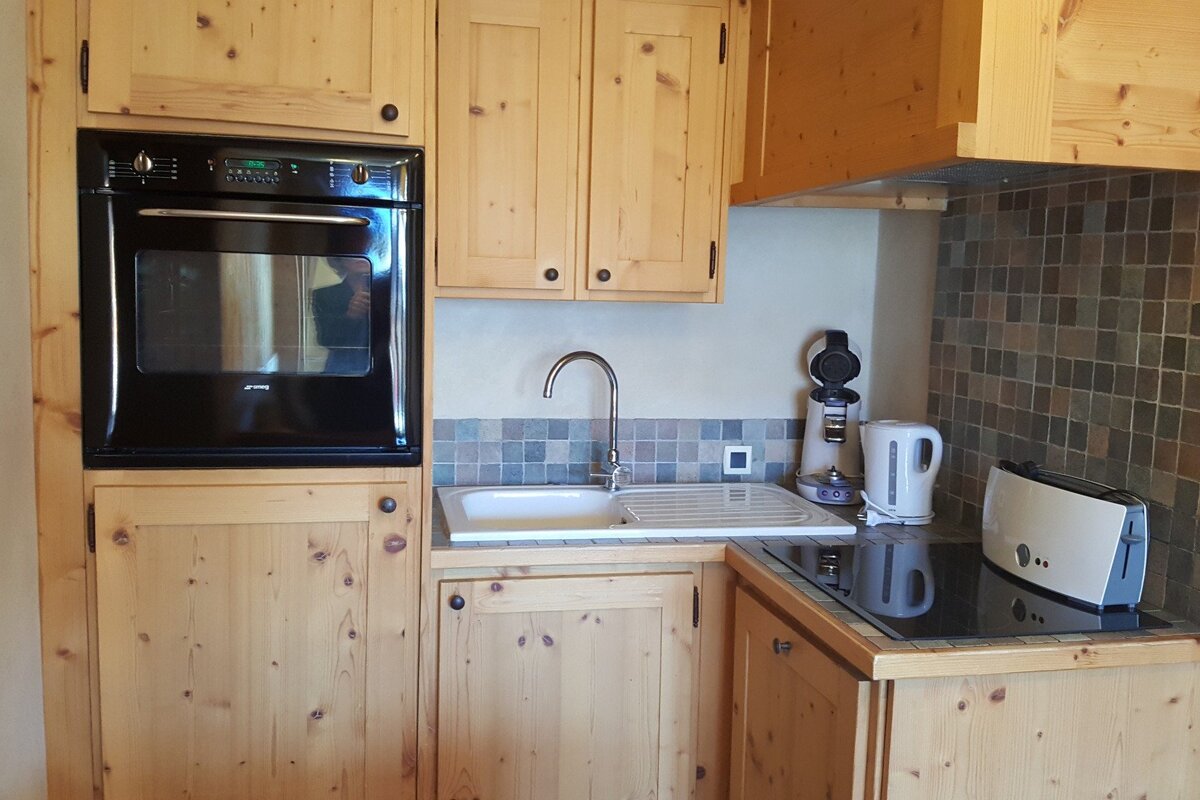 A kitchen with light wood cabinets, a built-in oven, sink, and tiled backsplash. Appliances include a coffee machine, kettle, and toaster.