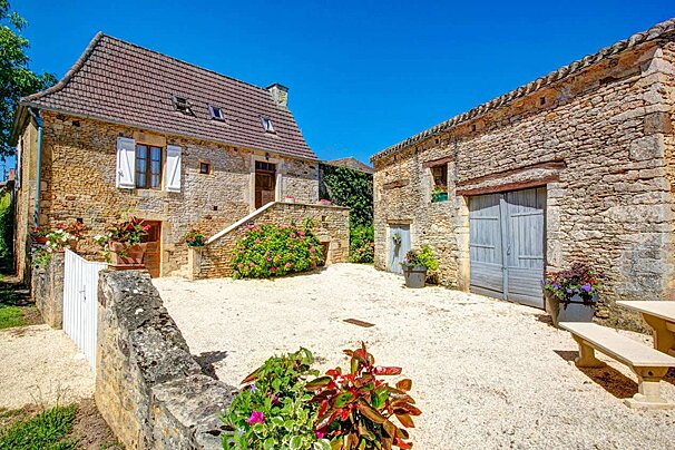 A stone house with a white fence and flowers in front of it