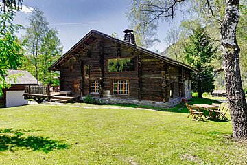 A large wooden house sits in the middle of a lush green field