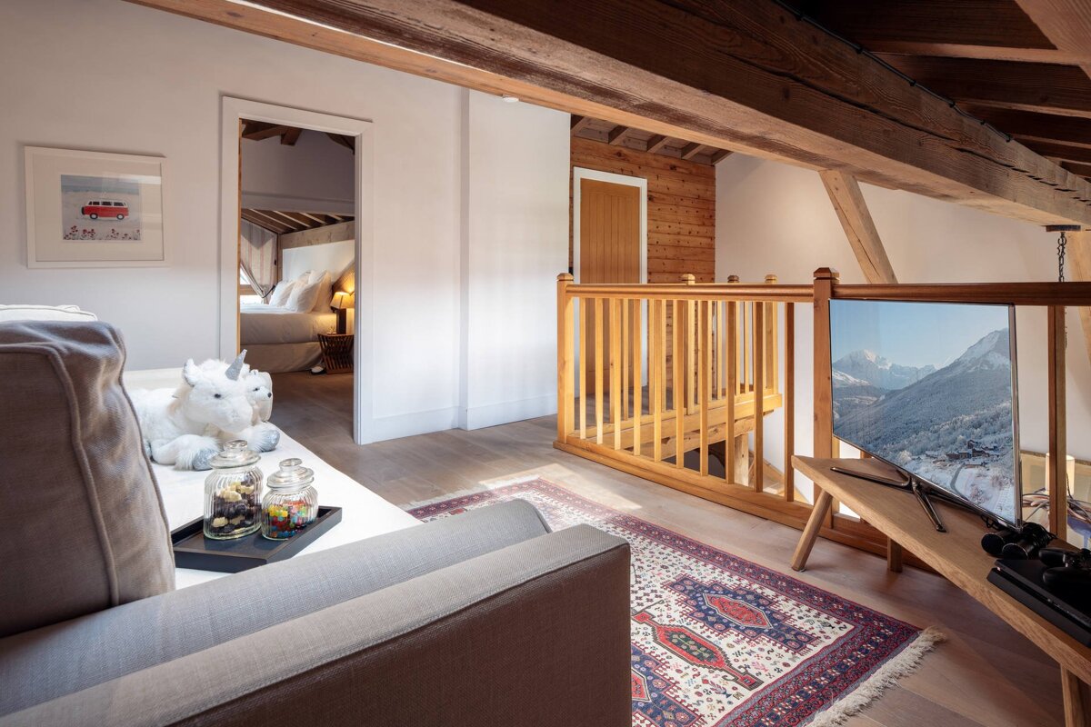 Cozy attic loft living area with a grey sofa, exposed wooden beams, a TV, and a doorway leading to a bedroom.