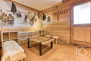 A cozy rustic mudroom with wood-paneled walls, ski-themed artwork, a wooden coffee table, storage shelves, and a bench with fur.