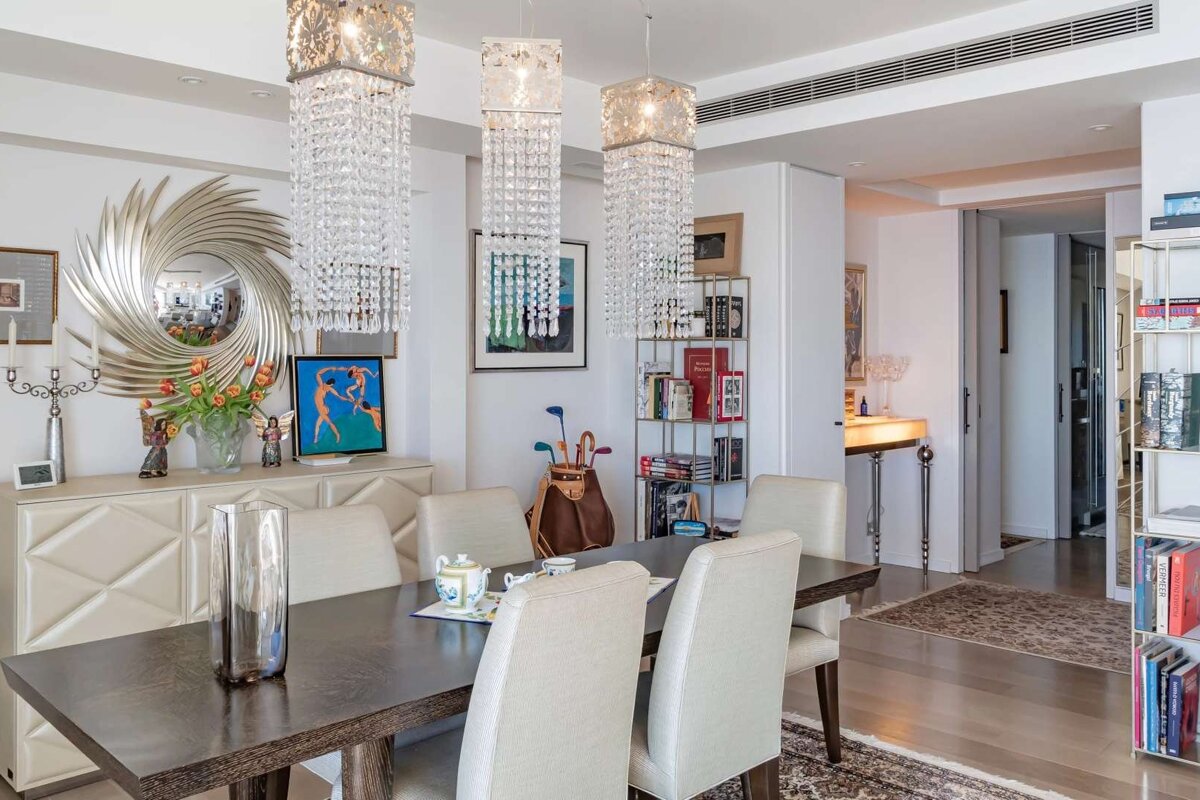 An elegant dining room featuring three sparkling crystal chandeliers, a dark wood table with upholstered chairs, a large decorative mirror, and bookshelves.