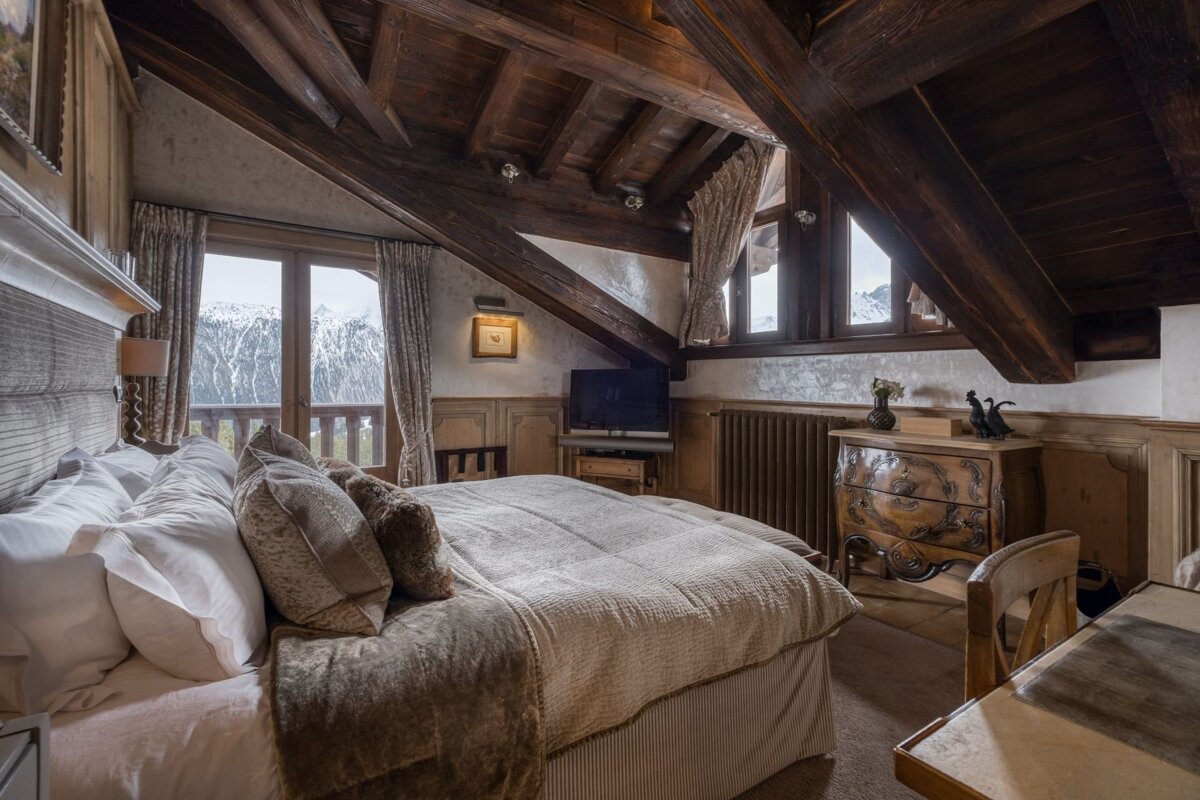 A rustic bedroom with exposed wooden beams, a plush bed, and a stunning mountain view from the balcony.