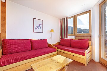 A cozy living room featuring two wooden daybeds with red polka dot cushions, a coffee table, and a window offering a mountain view.