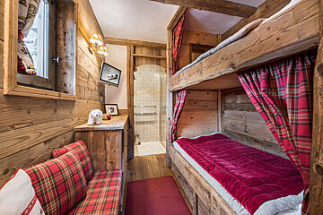 A bunk bed in a wooden cabin with red plaid curtains