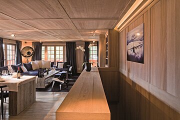 An elegant, wood-paneled room with a blue sofa living area, dining table, and large windows, bathed in soft light, offering a sophisticated retreat.