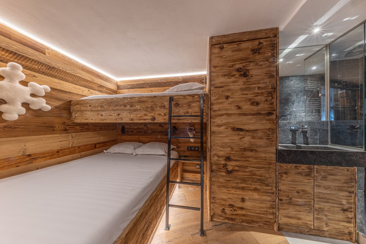 Rustic chalet bedroom with wooden bunk beds, a black metal ladder, and an integrated bathroom sink vanity.