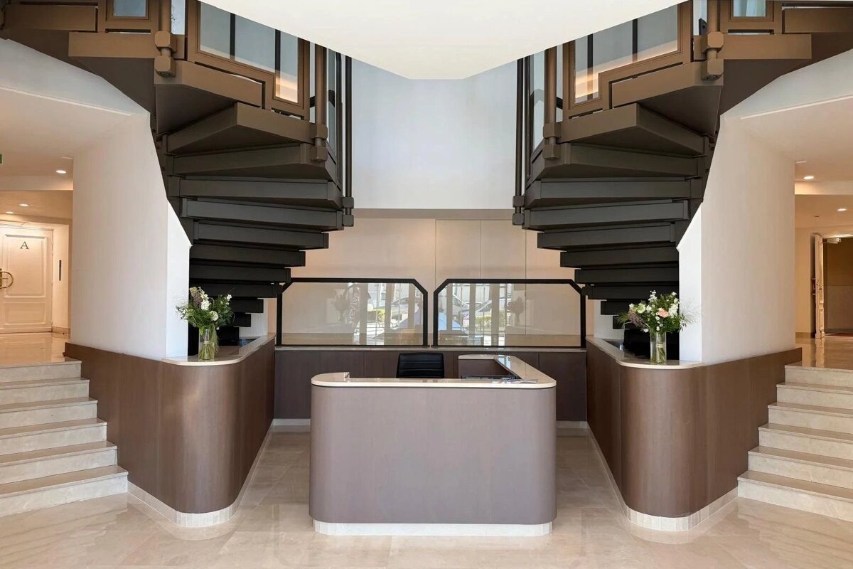 Symmetrical modern lobby with a central reception desk flanked by two dark spiral staircases.