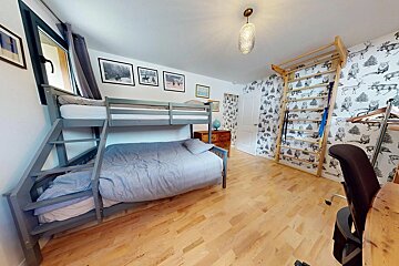 A children's room with a grey bunk bed, wooden floor, and a wall featuring black and white animal/forest wallpaper and a climbing frame.