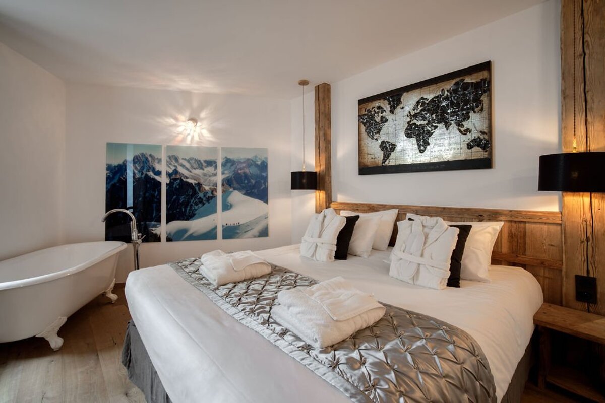 A modern bedroom with a large bed, clawfoot tub, mountain triptych, world map, and rustic wooden accents.