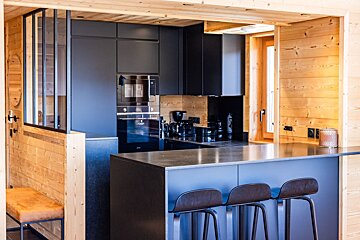 Modern chalet kitchen featuring dark blue cabinets, a breakfast island with three stools, and light wood paneling.