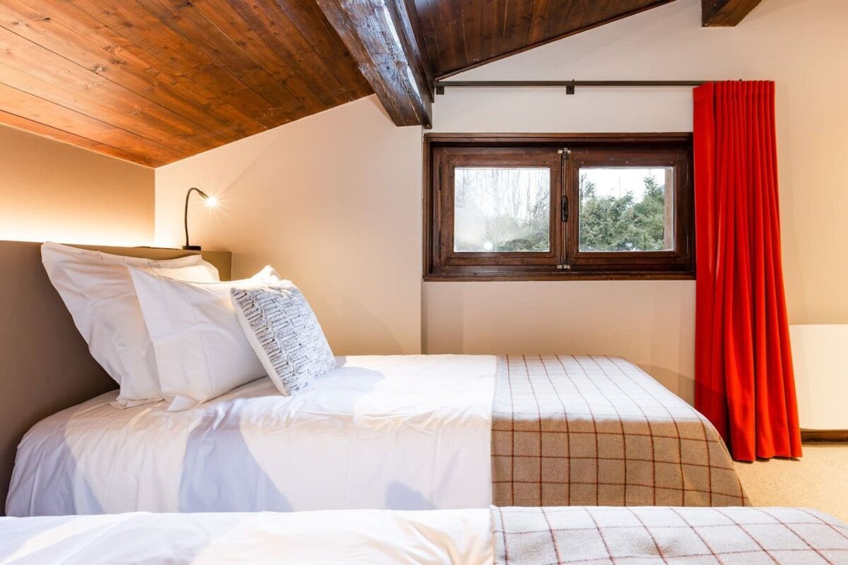 A bedroom with two beds and a window with a red curtain