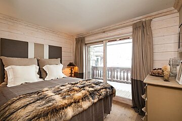 Cozy bedroom with a fur throw, wood paneled walls, and a sliding glass door leading to a snowy balcony view.