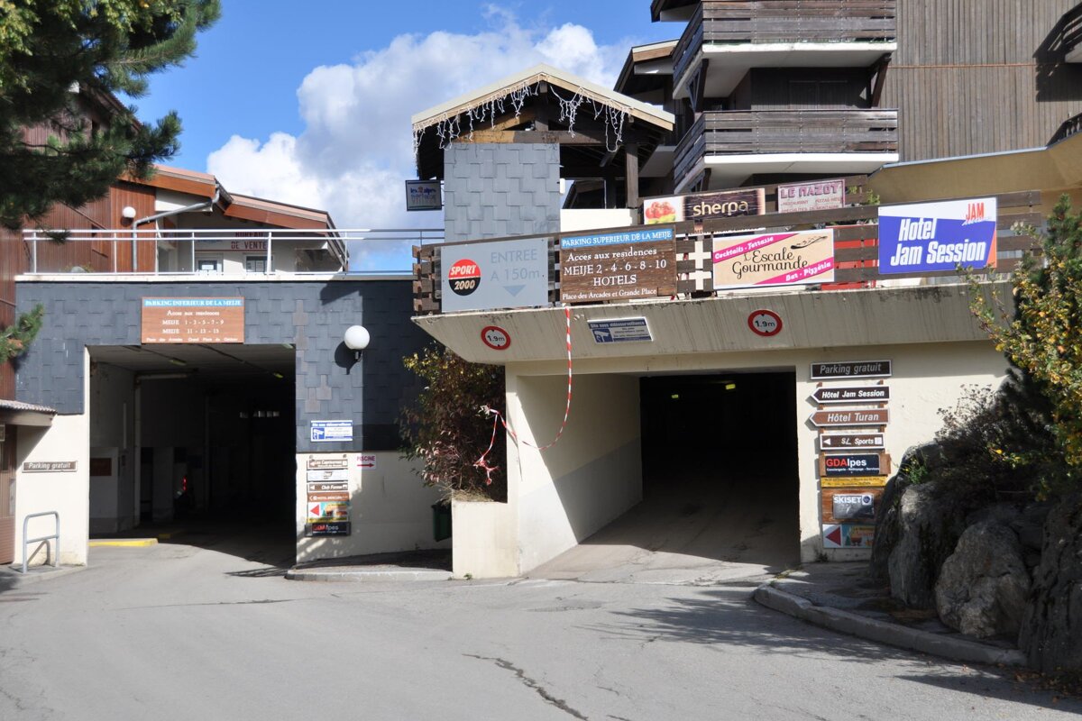Two underground parking entrances lead under buildings in a mountain resort, with numerous signs for hotels, shops, and parking directions.
