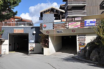 Two underground parking entrances lead under buildings in a mountain resort, with numerous signs for hotels, shops, and parking directions.