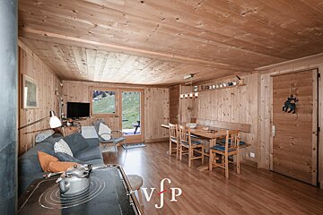 Cozy interior of a rustic wooden cabin featuring a living area with a sofa, a dining table, and a glass door leading outside.