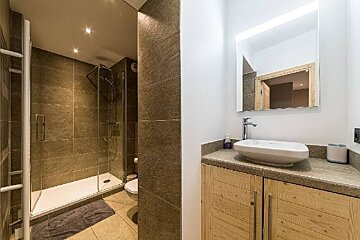 Modern bathroom with a glass walk-in shower, brown textured tiles, and a wooden vanity with a white vessel sink.