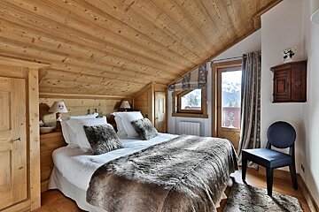 A bedroom with a large bed and a chair