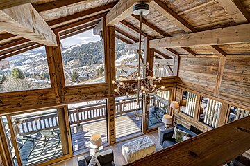 Cozy interior of a rustic wooden chalet with floor-to-ceiling windows overlooking a snowy mountain village.