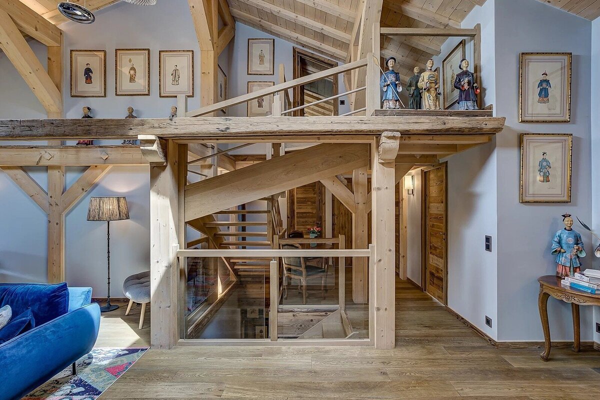 Timber-framed home interior featuring a wooden staircase, a loft with Asian figurines, and elegant rustic decor.