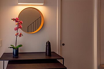 A vase of flowers sits on a table under a round mirror