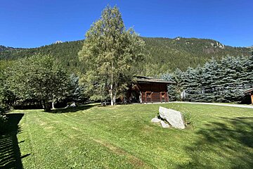 A house in the middle of a lush green field with mountains in the background