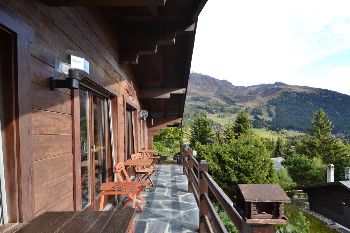 A balcony with tables and chairs and mountains in the background
