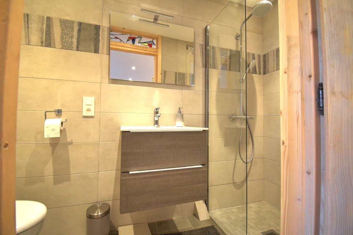 Modern bathroom featuring beige tiles, a floating wooden vanity, a large mirror, and a walk-in glass shower.