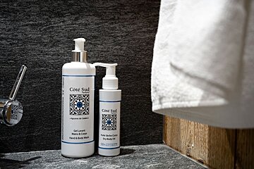 Two Côté Sud body wash and dry oil bottles sit on a dark bathroom counter, next to a chrome faucet and a white towel.