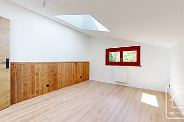 Bright, empty room with light wood floors, white walls, lower wood paneling, a red-framed window, and a skylight.