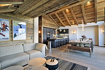 A rustic-modern open-plan living space with wood paneling, a sleek kitchen, dining area, and living room with ski posters.