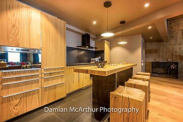 A sleek, modern kitchen featuring warm wooden cabinets, a chunky wood island with log stools, and ambient lighting, blending contemporary with rustic charm.