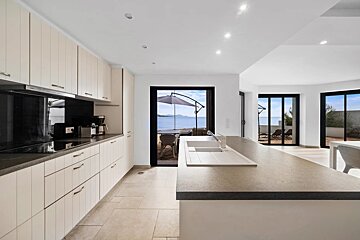 Modern white kitchen with island, facing sliding glass doors with a view of the sea and terrace.
