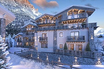A snow-covered alpine resort with warm, glowing lights set against a dramatic, snow-capped mountain at sunset.
