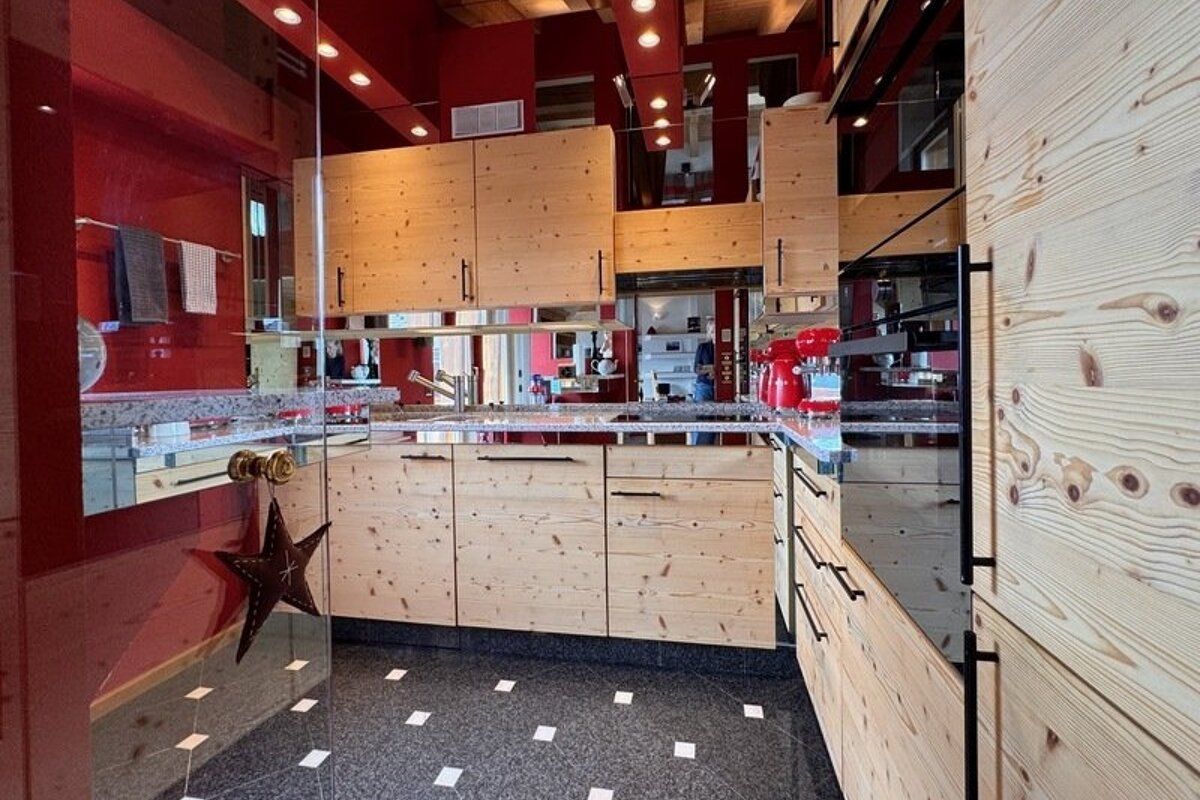 Modern kitchen featuring light knotty pine cabinets, vibrant red walls, and dark speckled tile flooring.