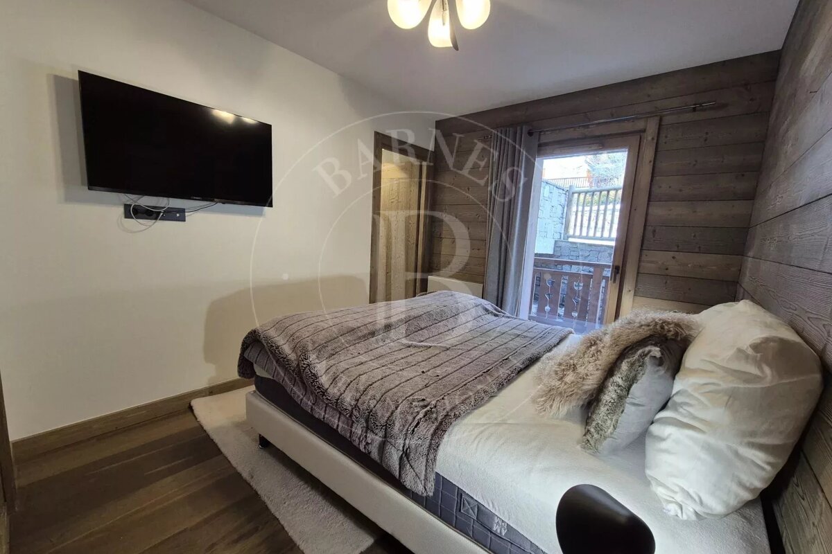 Cozy bedroom with a bed, wall-mounted TV, wooden accents, and a balcony visible through an open door.