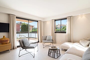 A modern living room with neutral tones, elegant armchairs, a white sofa, and glass sliding doors leading to a balcony.