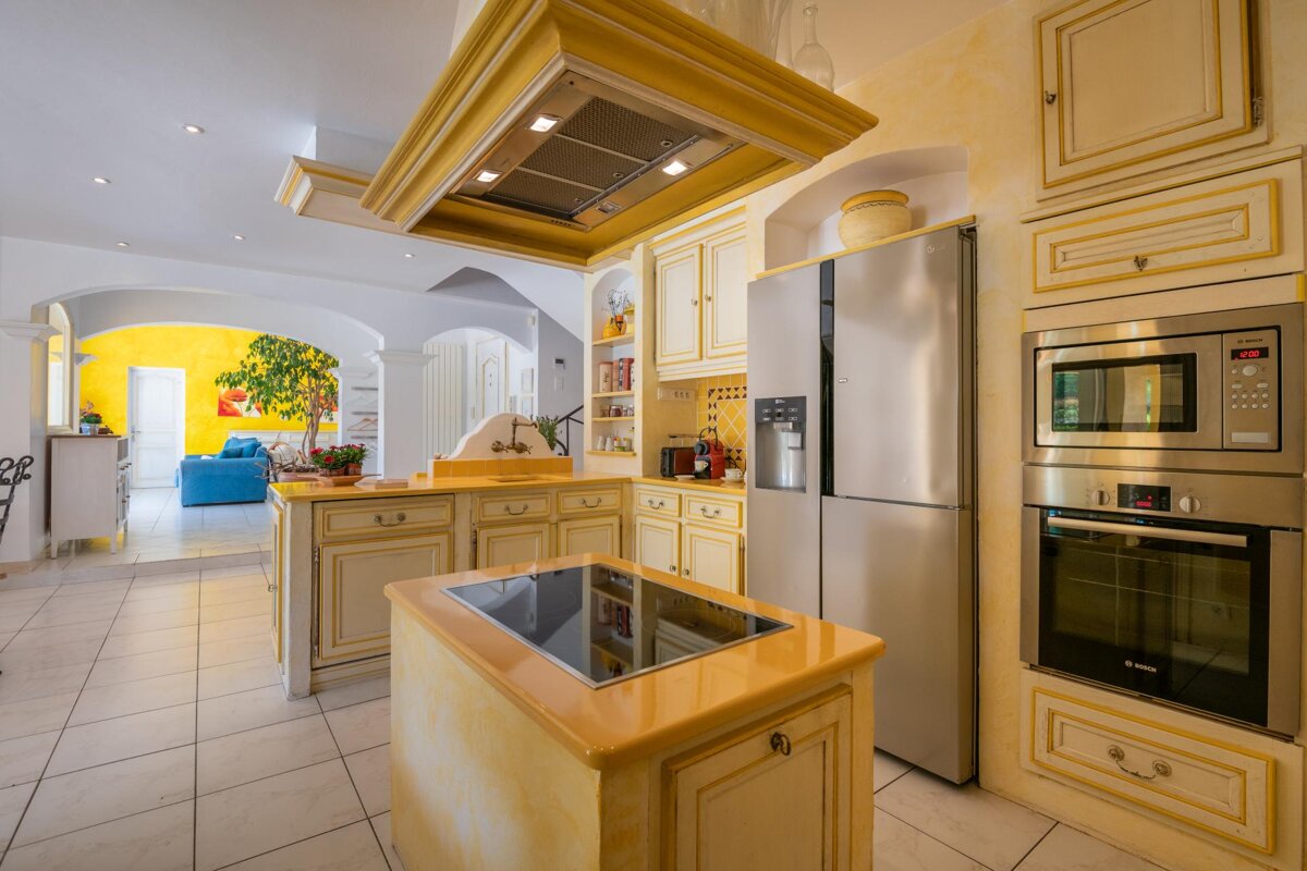 A kitchen with yellow cabinets and stainless steel appliances including a bosch oven