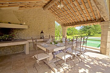 A table and chairs under a roof next to a pool