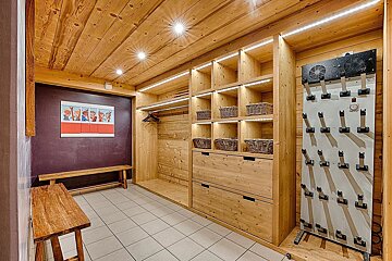 A cozy, wood-paneled ski room with a boot dryer, built-in shelves, storage baskets, benches, and bright lighting on a tiled floor.