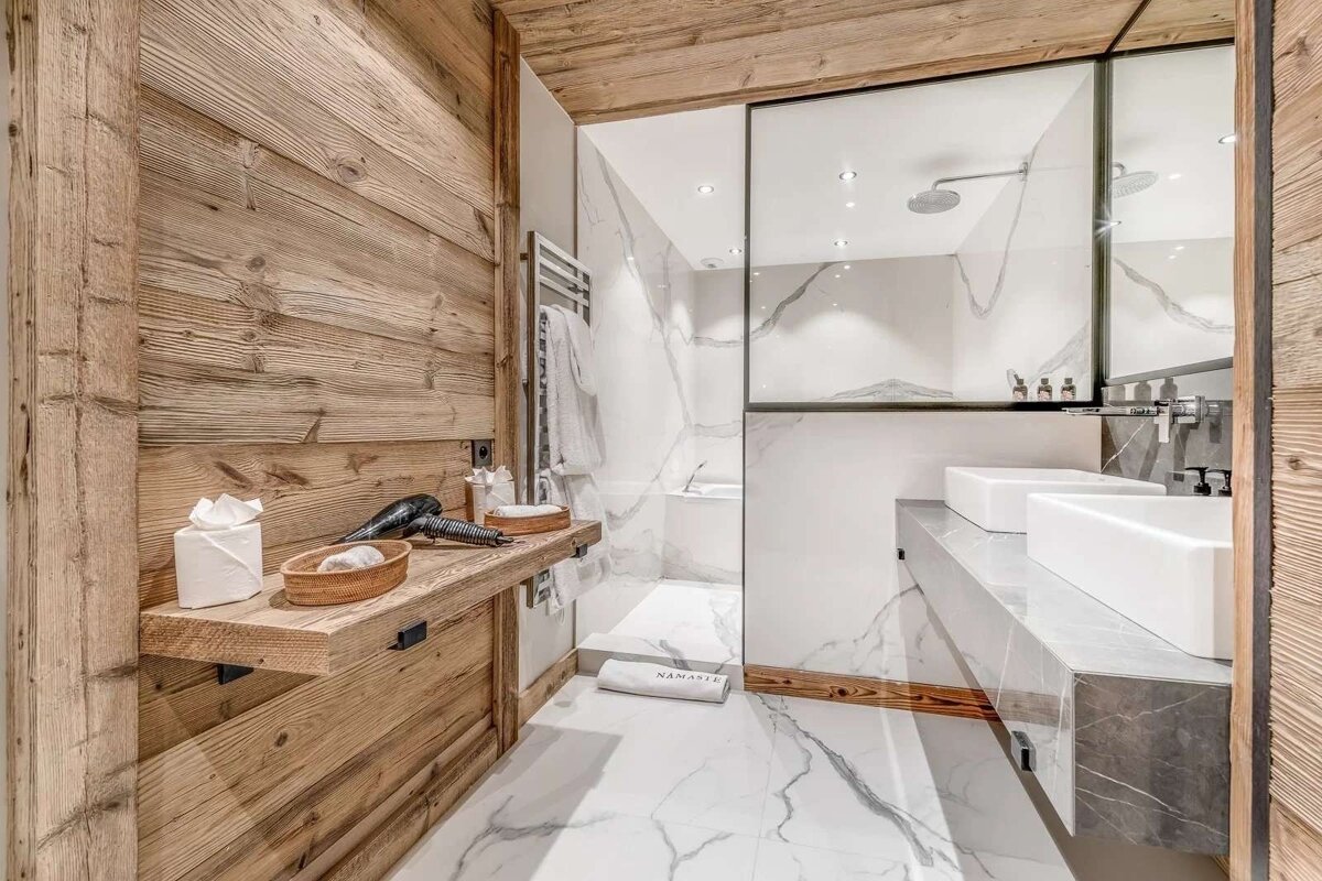 A luxurious modern bathroom featuring rustic wood paneling, white marble surfaces, a glass shower, and contemporary dual sinks.
