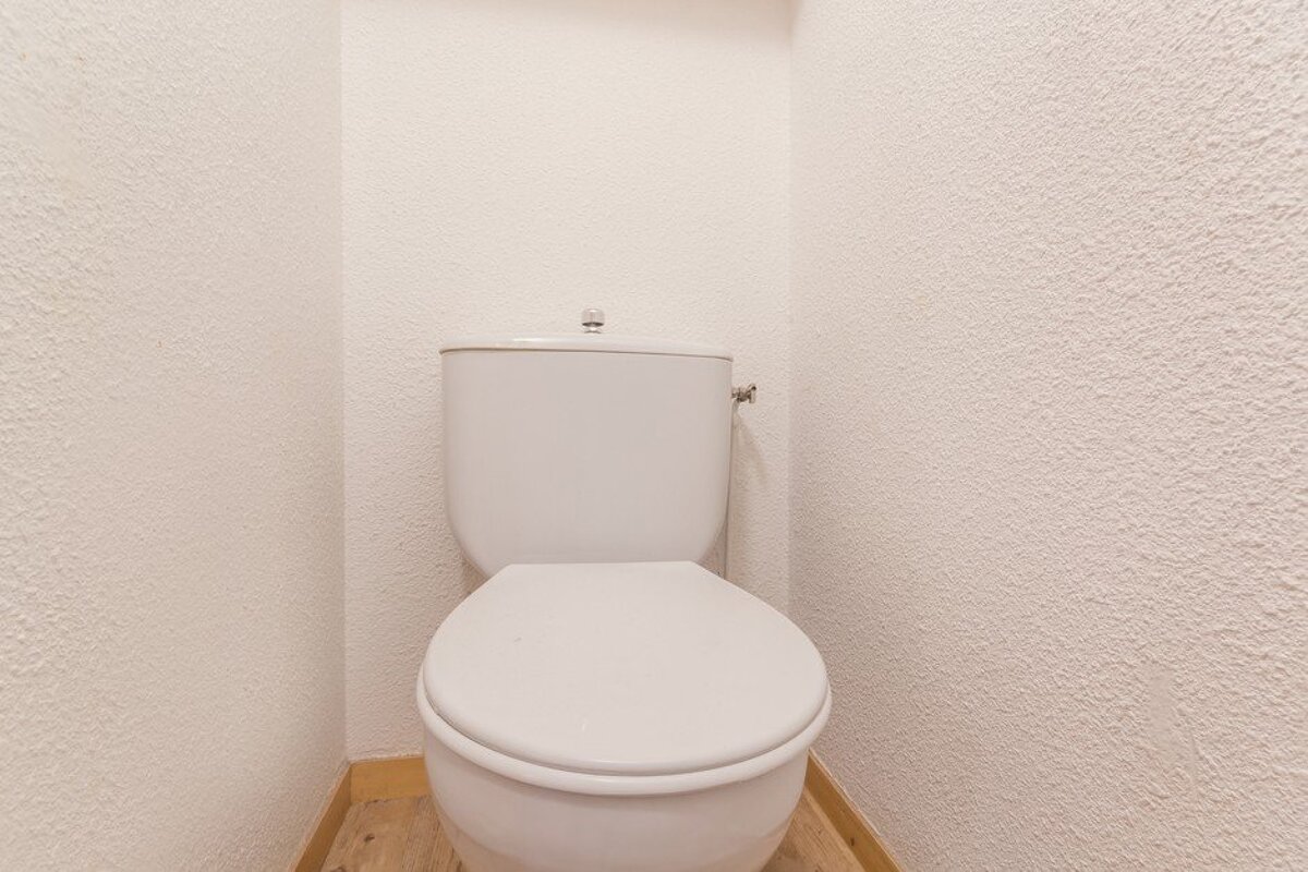 A toilet in a bathroom with a white wall