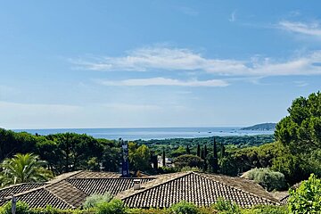 Lush green landscape and rooftop overlooking the calm blue sea under a partly cloudy sky.