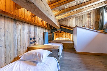 Rustic all-wood attic bedroom with exposed beams, sloped ceiling, and multiple beds, including a cozy, built-in sleeping nook.