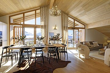 Bright, modern chalet interior with a dining table, living space, and large windows offering stunning snowy mountain views. Wooden accents enhance the alpine feel.