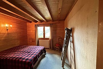 Rustic bedroom with wood walls & beamed ceiling. Features a red plaid bed, window with mountain view, and a leaning ladder.