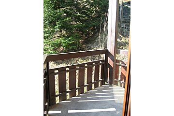 A balcony with a wooden railing and trees in the background