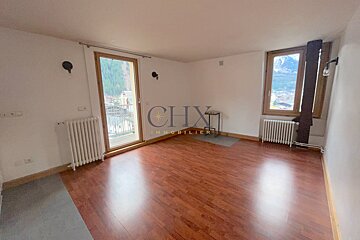 An empty room with reddish-brown wooden floors, white walls, a balcony door, and a window showing a mountain view.