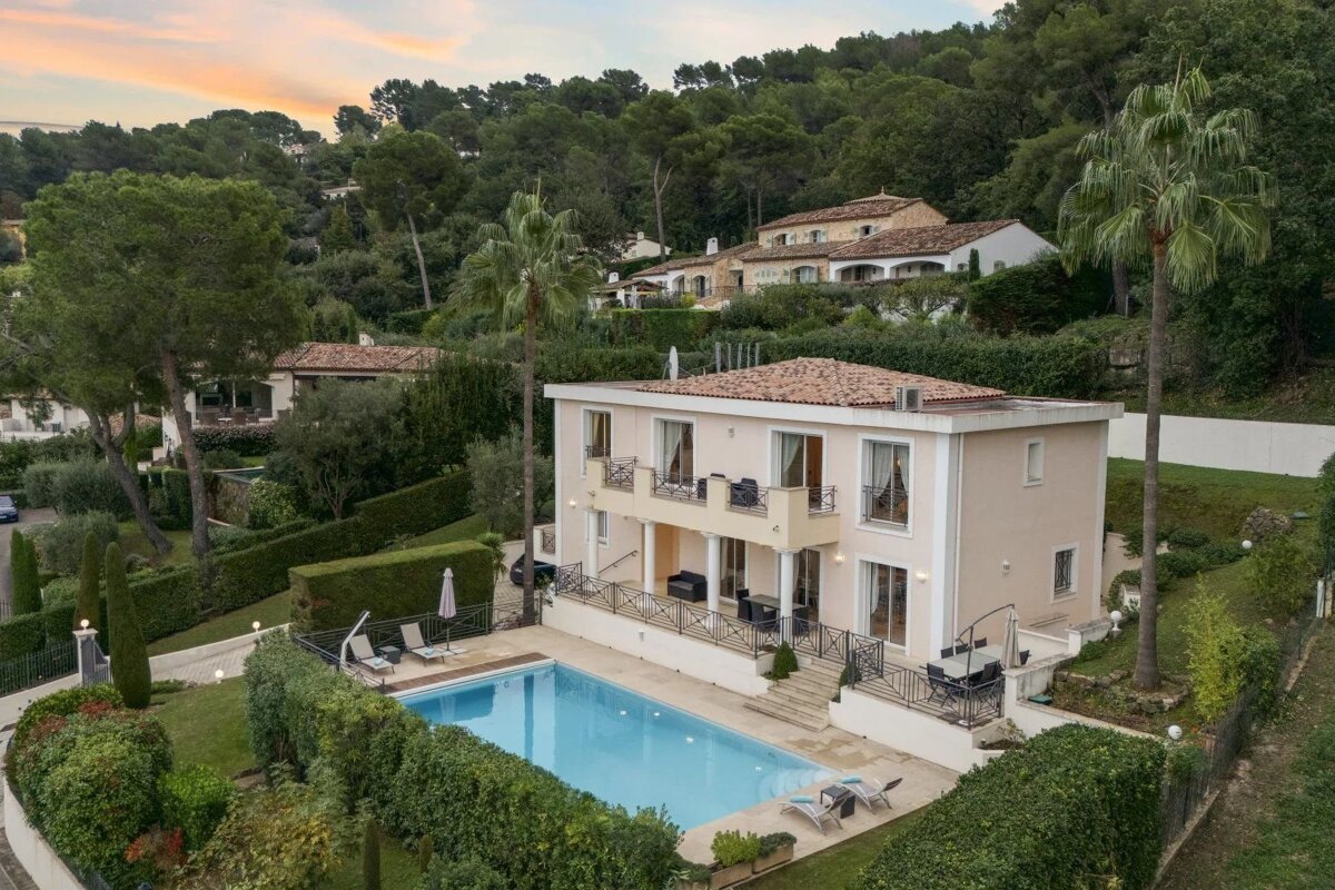Aerial view of a luxury villa with a swimming pool, nestled in lush green hills with palm trees.