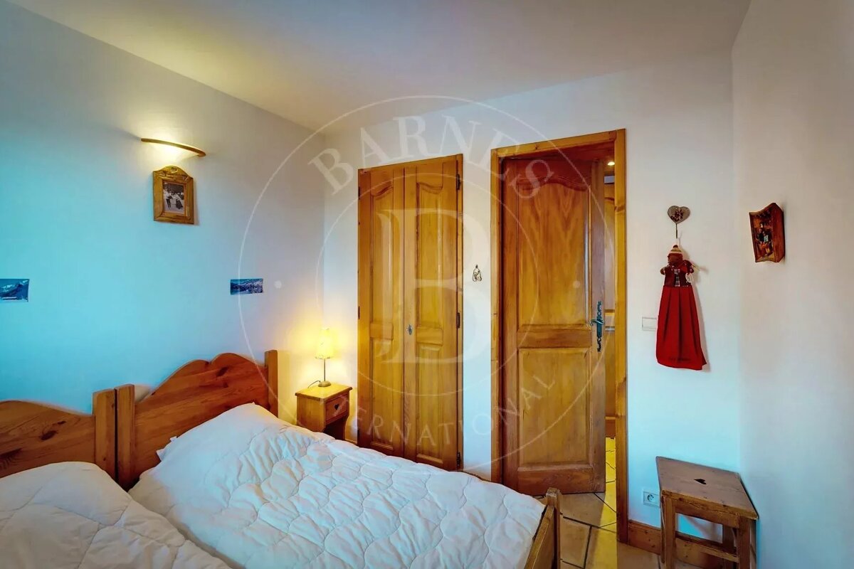 A cozy bedroom featuring two wooden single beds with white bedding, a wooden nightstand with a lamp, and two matching wooden doors. Minimal wall decor.